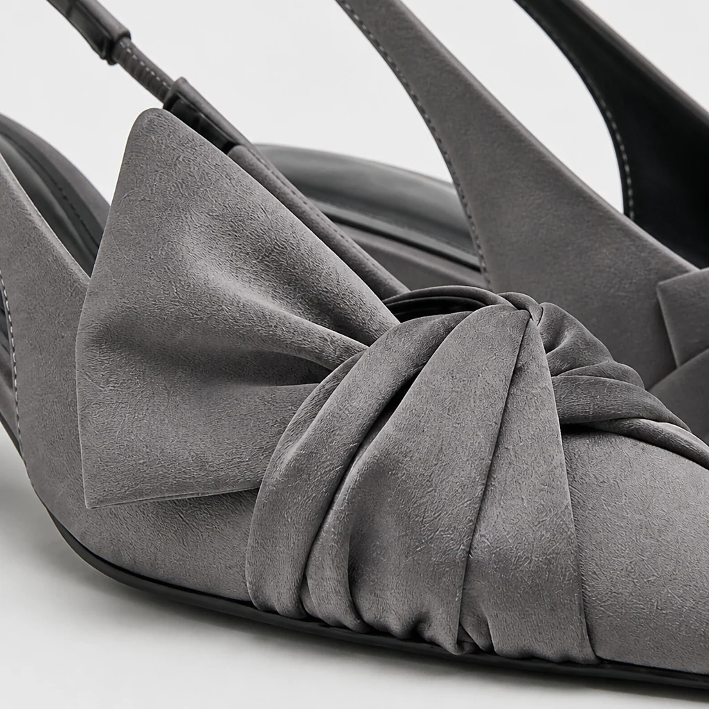 Primo piano del materiale grigio della décolleté slingback, dettaglio fiocco, punta appuntita e costruzione del tallone